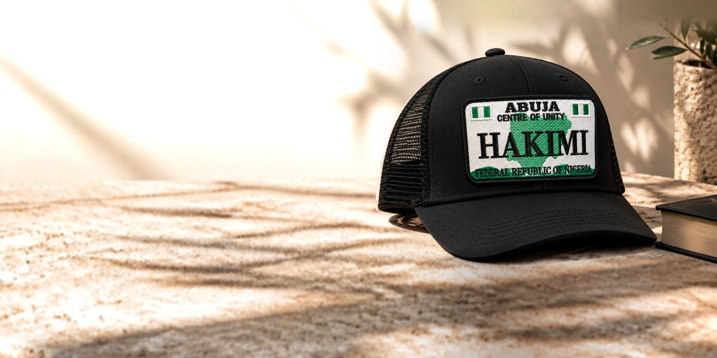 Black Point A trucker cap with the Abuja HAKIMI plate, resting on a sunlit stone ledge